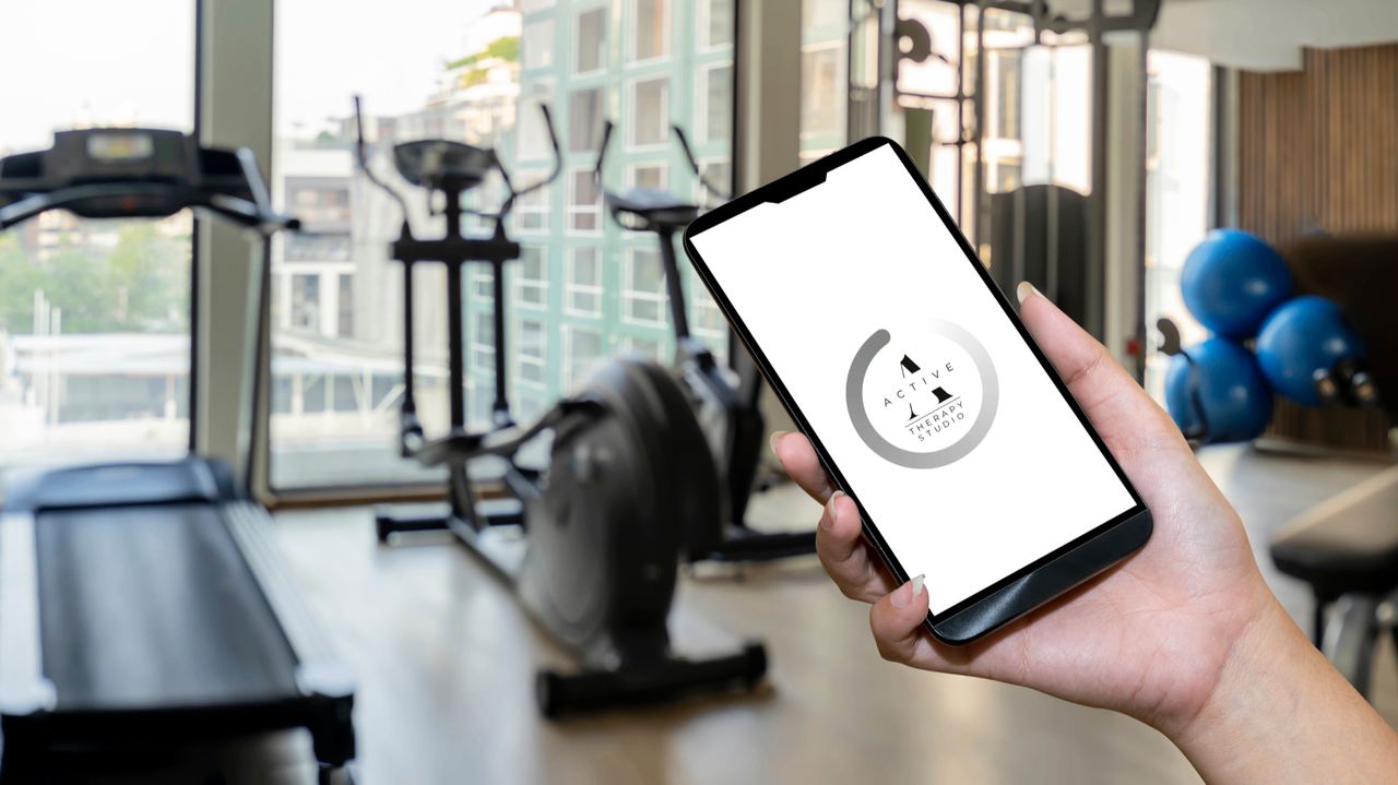 Aplikacja Active Therapy Studio na telefonie w tle siłowni